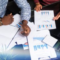 Part of hands of African-Americans in workflow with documents is top view. Various business colleagues sitting at table in modern office working with documents, calculators mobile phone. Can be used as business background