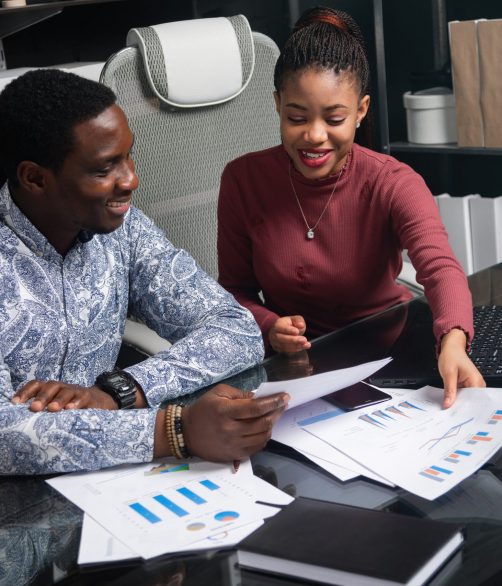 two young black people discuss their business using diagrams sitting at Desk in the office Various business colleagues sitting at table in modern office talking together. An African-American businessman and entrepreneur have an informal meeting in Cabinet. Two friendly black young men understand financial documents at Desk